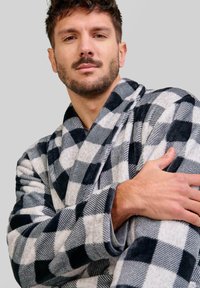 Bata de franela a cuadros en negro y gris con cuello, textura suave y mangas anchas. La tela presenta patrones alternos de cuadros sólidos y rayados.