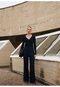 Cardigan aderente blu navy con scollatura a V e bottoni, abbinato a pantaloni a gamba larga. Tessuto liscio dal design minimalista; borsa a spalla inclusa.