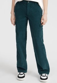 Teal corduroy cargobroek met brede benen, voorzien van zijzakken en een knoopsluiting, gecombineerd met zwart-witte sneakers.