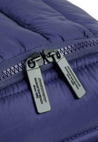 Tejido de chaqueta acolchada color marino con textura acolchada; presenta dos cremalleras negras con etiquetas de marca y costuras a juego a lo largo de las costuras.