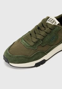 Roheline tennisejalats, mis ühendab seemisnahast ja tekstiilist materjale, ümar kuju, paksud paelad ning kontrastne valge vahtpõhi musta tallaga.