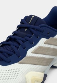 Chaussure de sport bleu marine et blanche avec une tige en mesh texturé, des lacets plats et des accents beige sur le côté et la semelle.