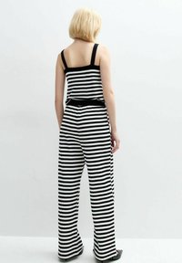 Randig stickad jumpsuit i svart och vitt med vida ben, breda axelremmar och en figursydd midja. Slät textur och avslappnad passform.