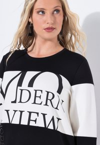 Schwarz-weißes Oberteil mit auffälligem Text "MODERN VIEW." Es hat einen runden Ausschnitt, lange Ärmel und eine glatte Baumwolltextur.
