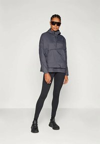 Temno siva, lahka pulover jakna z visokim ovratnikom in zadrgo. V kombinaciji s črnimi leginami in črnimi športnimi čevlji.