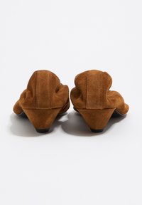 Mocasines de ante marrón con punta puntiaguda y tacón cónico, con detalles plisados en la parte trasera que le dan una apariencia texturizada.