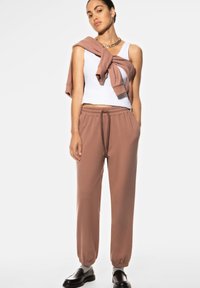 Lichtgewicht witte tanktop, roze joggerbroek met een elastische tailleband en manchetten, en een roze sweatshirt over de schouder gedrapeerd.