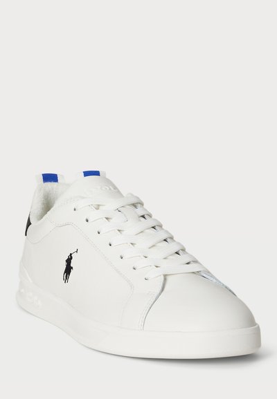 Biele kožené tenisky s okrúhlou špičkou, so čiernym logom, bielymi šnúrkami a modrými akcentmi na jazyku a päte.