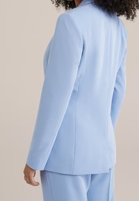 Ljusblå skräddarsydd kavaj med strukturerade axlar, slät tyg och rena linjer, med långa ärmar och en enda baksidesventil.