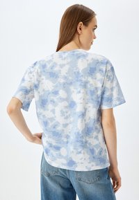 Camiseta de algodón en azul claro con un patrón de nubes, mangas cortas y un escote redondeado, combinada con jeans azules.