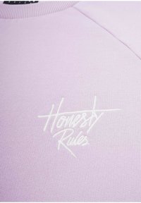 Vaaleanlila collegepaita, jossa on ribatattu kaula-aukko ja raglan-hihat. Kuvassa on valkoisella brodeerattu teksti "Rehellisyys Sääntöä." Miellyttävä pinta.