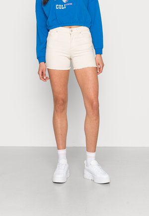Shorts de mezclilla color crema con dobladillo deshilachado, combinados con un sudadera azul. Modelo lleva zapatillas de plataforma blancas y calcetines hasta el tobillo.