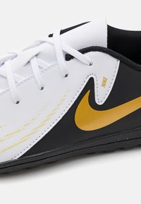 Calzado Nike con un diseño en blanco y negro, con un logotipo de swoosh dorado, material texturizado y cordones en contraste sobre una suela moldeada.