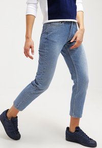 Ljusblå raka jeans i denim, med en klassisk fem-fickors design och fransade kanter, matchat med blå sneakers.