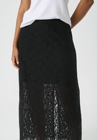 Schwarzer Spitzen-maxikleid mit floralen Mustern, ausgestattet mit einer taillierten Taille und transparenter Textur, geschichtet über einem einfarbigen schwarzen Futter.