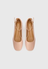 Nude patent leather shoes with a rounded toe, ankle strap, and cushioned insoles. Simple design, smooth texture, and minimal accents.
