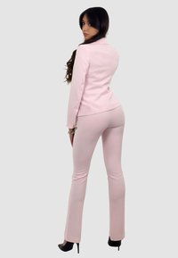 Blazer rosa e pantaloni aderenti realizzati in tessuto liscio. L'outfit presenta un design su misura, dettagli con spacco sul retro e gambe slim svasate.