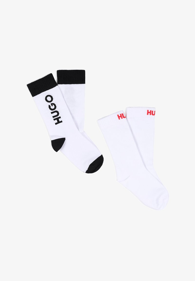 Deux paires de chaussettes blanches, l'une avec un bord, un orteil, un talon noirs et le texte "HUGO", l'autre avec un bord blanc et un texte partiel "HUGO" en rouge.