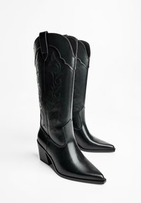 Black leather cowboy boots with pointed toes, decorative stitching along the sides, and a block heel. Smooth texture and tall design.
