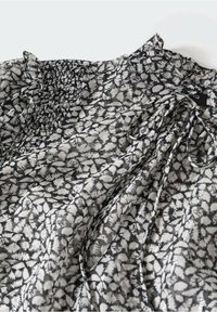 Blouse à motif floral noir et blanc avec un corsage froncé, col volanté et tissu léger et fluide.