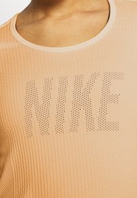 Trenérková košile v broskvové barvě s textura vzorem a perforovaným logem "NIKE". Obsahuje kulatý výstřih a přiléhavý střih.