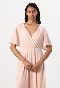 Rochie roz deschis, fluidă, cu decolteu adânc în V și mâneci scurte în volan. Confecționată dintr-un material moale, cu talie strânsă și o croială lejeră.