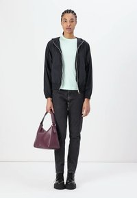 Giacca bomber nera con zip sopra una maglia leggera color menta, abbinata a jeans scuri e stivali neri stringati. Tiene una borsa a tracolla bordeaux con una tracolla larga.