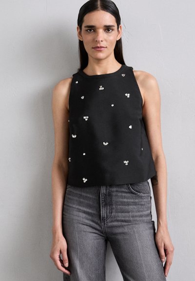 Črn brezrokavnik s skrajšanim dizajnom, okrašen s srebrnimi dodatki. Usklajen z hlačami z visokim pasom v sivi barvi, kjer je vidna tekstura denima.