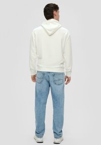 Sudadera blanca con capucha y puños acanalados, combinada con jeans de mezclilla azul claro que cuentan con dos bolsillos traseros y un diseño desvanecido.