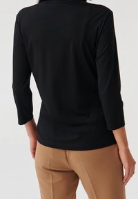 Black long-sleeve top with a fitted design and a smooth texture, paired with brown textured trousers. Simple, clean lines.