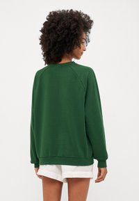 Sweatshirt verde cu o croială confortabilă, mâneci raglan și manșete cu reiat. Textură moale, având un interior neted și un guler clasic de tip crew.