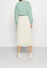 Felpa cropped verde menta, gonna midi plissettata avorio e sneakers chiare con dettagli, viste da dietro su uno sfondo bianco.