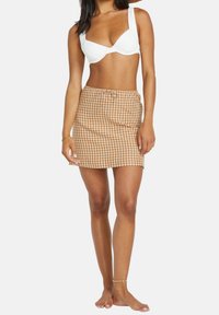 Mini falda de cuadros marrones y blancos con cintura ajustable, fabricada en tejido ligero, con un corte recto y textura suave.