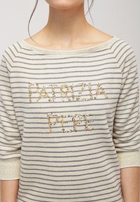 Sudadera a rayas en crema y gris, con un logo de lentejuelas doradas "PATRIZIA PEPE" en el frente y un escote ligeramente desviado del hombro.