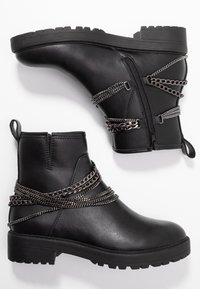 Botines negros de tobillo hechos de cuero sintético con un acabado texturizado. Cuentan con detalles de cadena metálica y una cremallera lateral para facilitar su uso. Suela plana y robusta.