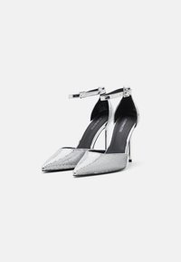 Zilveren pailletten hoge hakken met puntige neuzen, enkelbandje en stiletto-hakken. Zwarte binnenvoering, elegante vormgeving, metalen accenten.