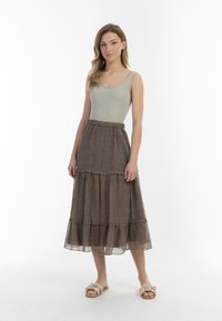 Ribbede, lysegrønne top med stropper parret med en lagdelt, ankellang brun nederdel med et lille mønster og bølgede kanter. Bruges med beige flade sandaler.