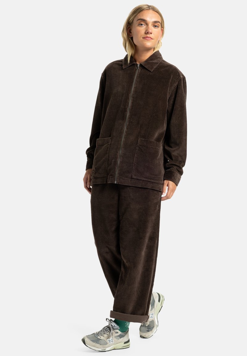 Brown corduroy jacket with a zip front, large pockets, and a collar, paired with matching corduroy pants and gray sneakers.