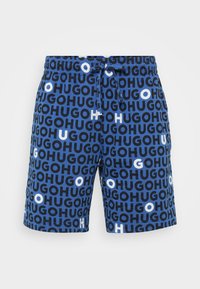 Shorts bleus avec un imprimé intégral du mot "HUGO" dans des tailles et des couleurs variées, dotés d'une taille avec cordon de serrage et d'une texture de tissu doux.
