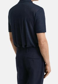 Polo marine à manches courtes, en tissu texturé, associé à un pantalon foncé avec des poches arrière à double bouton.