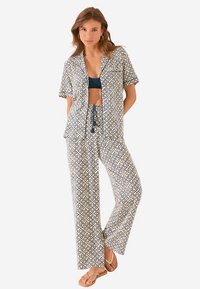 Leichtes, gemustertes Pyjama-Set in Marineblau und Creme; kurzärmeliges Oberteil mit Kragen, Hose mit Kordelzug, lockere Passform, getragen mit Flip-Flops.