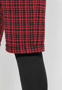 Röda och svarta rutig shorts med guldstickningar, med uppvikt nederkant, ihop med åtsittande svarta leggings. Texturerad tyg syns.