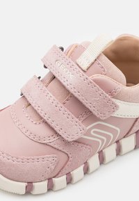 Zapatillas infantiles rosas que combinan materiales de ante y sintéticos, con dos correas de velcro y una suela texturizada con acentos en blanco y morado.