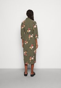 Olivgrünes Blumenkleid mit Dreiviertelärmeln, taillierter Taille und einer Länge bis zur Mitte der Wade. Es hat ein Muster aus mehrfarbigen Blumen.