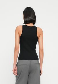 Haut noir sans manches avec une coupe ajustée, une texture côtelée et un col rond. Associé à un pantalon gris à jambes larges, vue de dos.