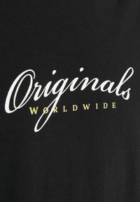 Sort bomuldsstof med hvid tekst "Originals" i kursiv og ordet "WORLDWIDE" i guld nederst. Glat tekstur, enkelt design.