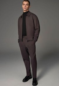 Brown textured jacket with matching trousers, complemented by a black turtleneck. Fitted design and black shoes. Simple, modern silhouette.