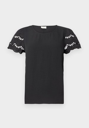 Blouse noire à manches courtes texturée avec des manches en dentelle découpées en forme de vagues et un col rond sur fond blanc.