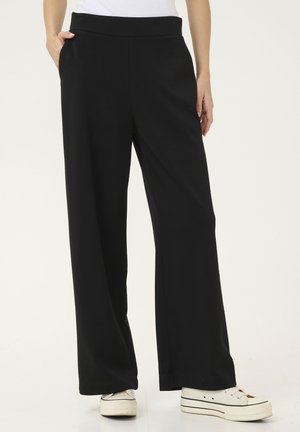 Black wide-leg trousers made of soft, stretchy fabric. Features a high waist and side pockets, paired with white sneakers.