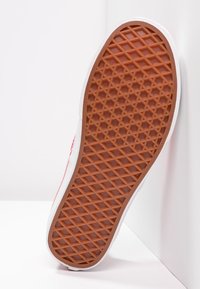 Rød og hvit sneaker-såle med en teksturert gummisåle, som har et diamantmønster for grep og en avrundet form.